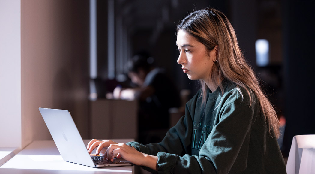 Young female sits in dimly lit office space on a laptop