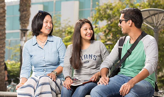 Three international students smiling and talking while sitting outside on campus