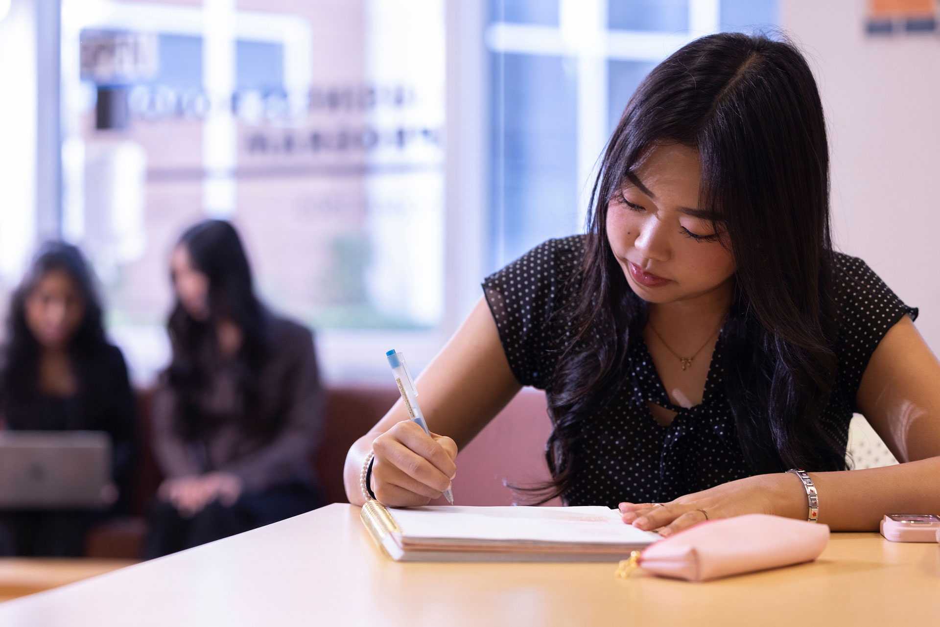 A femal Asian student writing in her notebook indoors.
