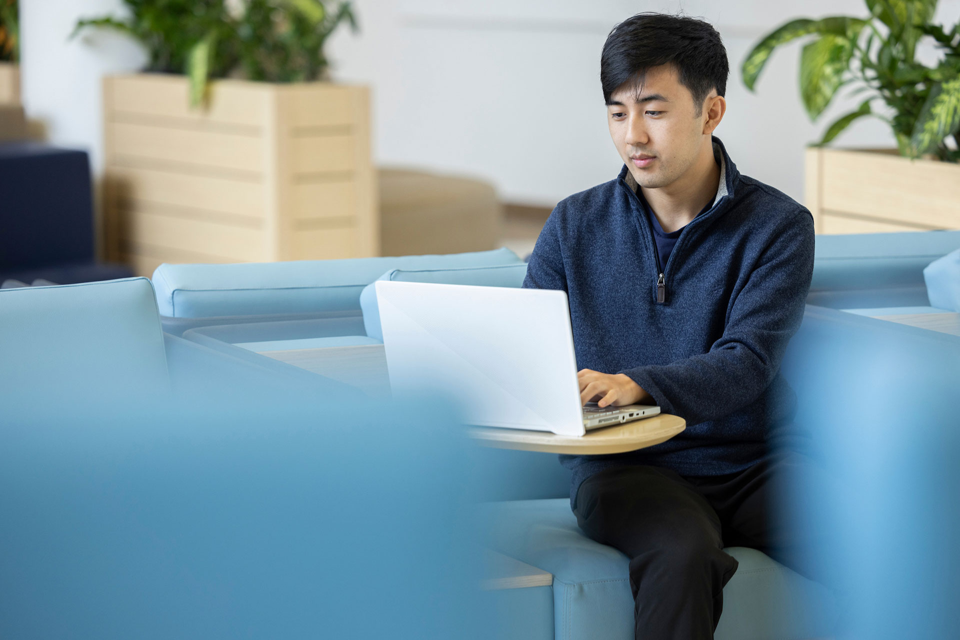 A male student working on his laptop while sitting comfortably in a chair.