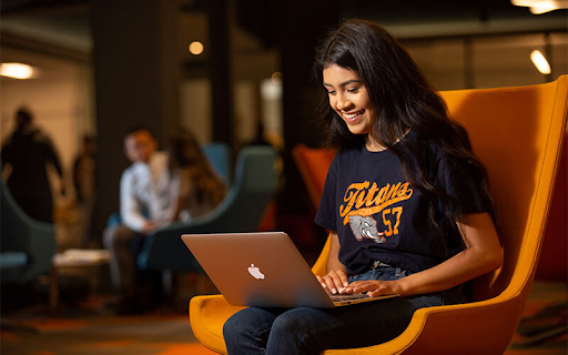 Female student sitting in the Pollak Library lounge area with a laptop