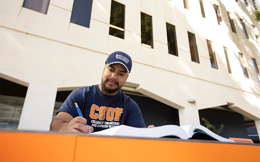 Male CSUF student doing homework at an orange table outside the CSUF College of Engineering building